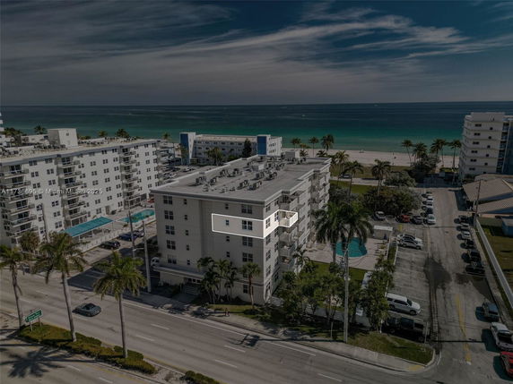 Aerial view of a multi-story beachfront building with a pool and parking area.