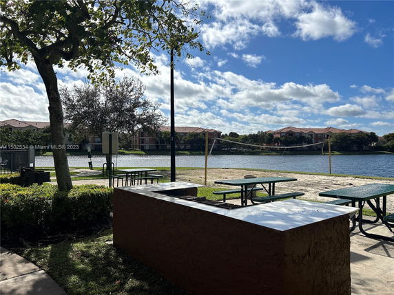 View of a lake with a volleyball court and picnic tables in a residential area.