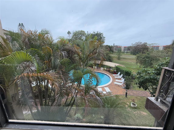 View of an outdoor swimming pool surrounded by palm trees and lounge chairs.