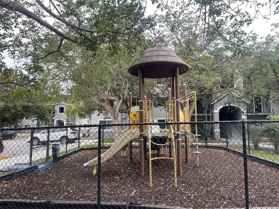Playground with slides and climbing structures surrounded by trees and a fence.