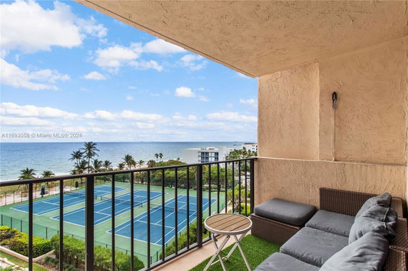 Balcony view overlooking a tennis court, ocean, and palm trees.