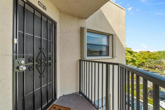 Balcony view with metal railings and entrance door to an apartment, overlooking a parking area and trees.