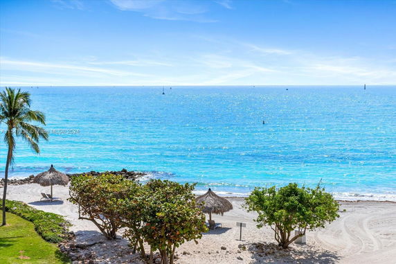 View of a sandy beach with a palm tree and ocean in the background.