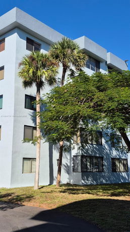 Front view of a multi-story residential building with several windows and trees nearby.