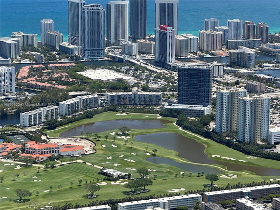 Aerial view of high-rise buildings near a golf course and the ocean.
