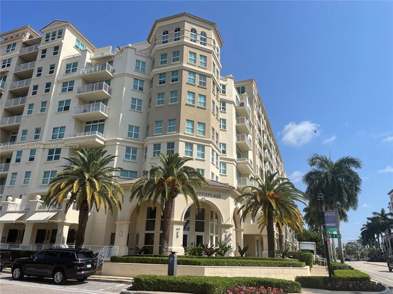 Front view of a multi-story apartment building with balconies and palm trees.