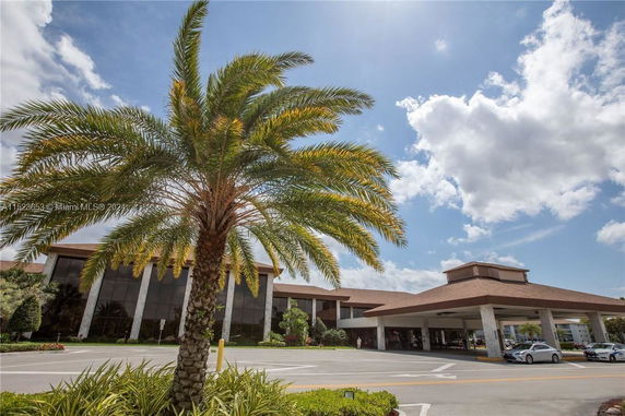Front view of a large building with a covered entrance and palm tree in foreground.
