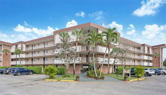 Front view of a multi-story residential building with balconies and palm trees.