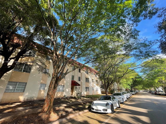 Front view of a multi-story building with trees along the street and cars parked in front.
