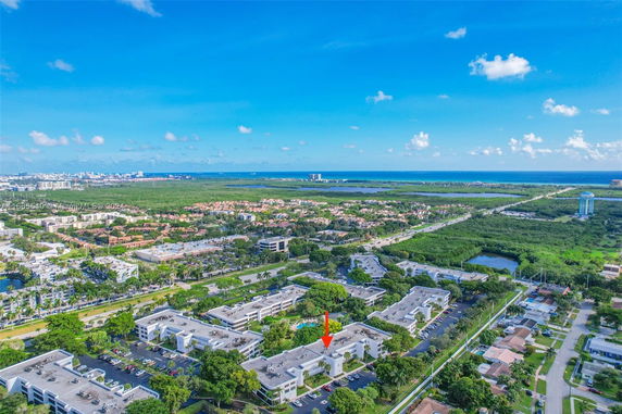 Panoramic view of a residential and commercial area with greenery and distant ocean.