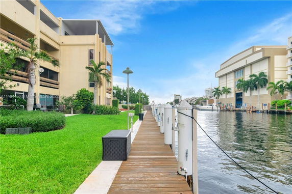 Buildings next to a waterway with a wooden dock and green lawn.