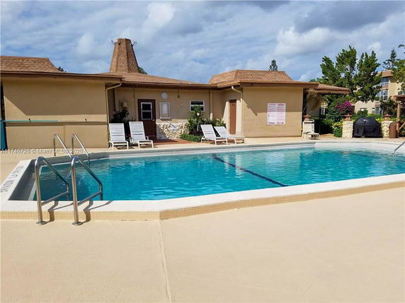 Outdoor swimming pool with adjacent building and lounge chairs.