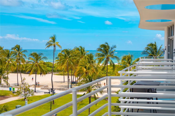 Balcony view overlooking beach and palm trees with ocean in the background.