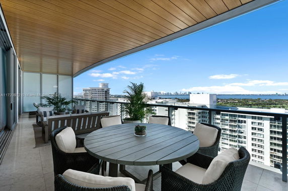 A balcony with a wooden ceiling and outdoor furniture offering a wide view of city buildings and a distant waterfront.