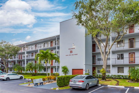 Front view of a multi-story apartment building with balconies and a parking area.
