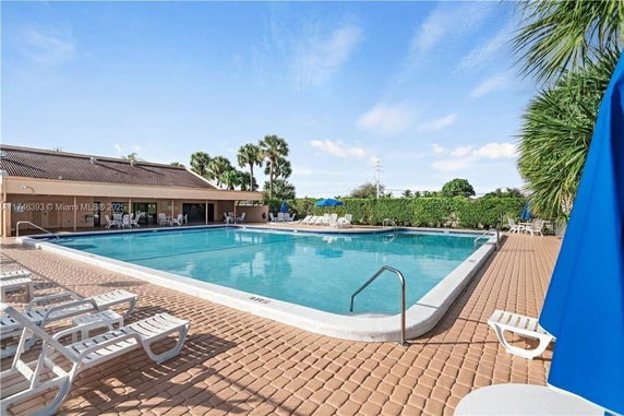 Outdoor view of a swimming pool area with lounge chairs and a building in the background.