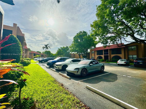 Outdoor parking area with several cars parked in front of residential buildings.