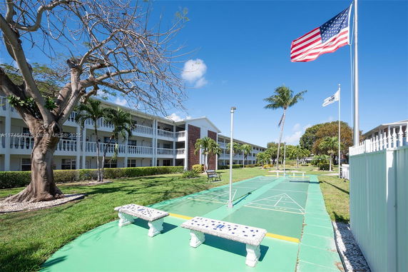 View of a residential building with balconies, surrounded by greenery and flags in the foreground.