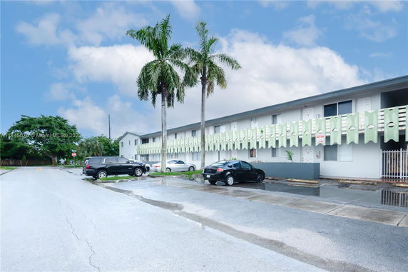 Outdoor parking area in front of a two-story building with palm trees.