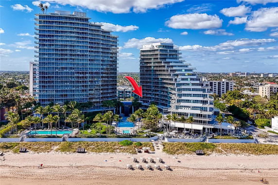 Front view of two modern high-rise buildings with balconies and a swimming pool area in front, located by the beach.