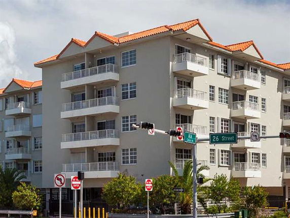Front view of a multi-story apartment building with balconies and a red-tiled roof.