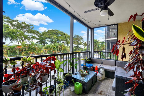 Balcony with plants and seating area overlooking trees and sky.