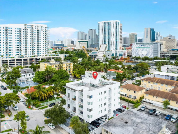 Aerial view of a mid-rise residential building surrounded by taller skyscrapers and other urban structures.