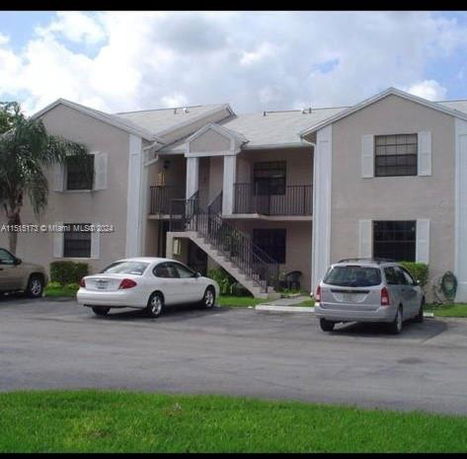 Front view of a two-story apartment building with exterior stairs and parked cars.
