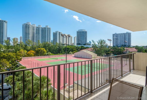 View from a balcony overlooking tennis courts and tall buildings in the background.