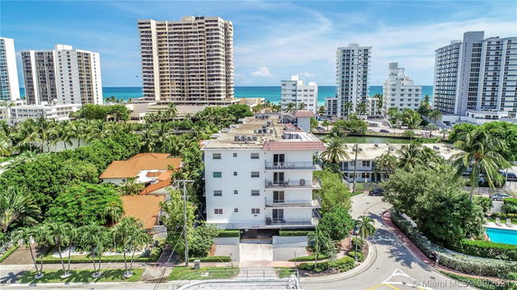 Aerial view of a mid-rise apartment building surrounded by taller residential buildings near the ocean.