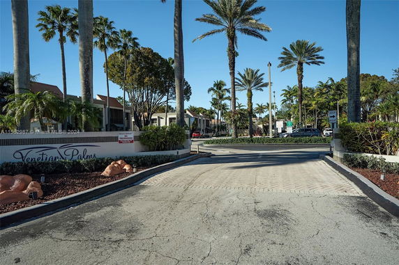 Front view of a residential complex with palm trees and a driveway entrance.