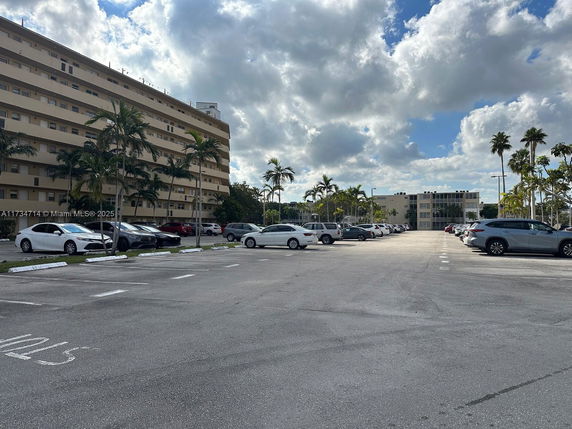 Outdoor parking area with multiple cars parked near a multi-story building.