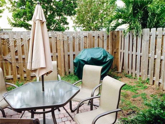 Outdoor patio area with table, chairs, and a barbecue grill surrounded by a wooden fence.