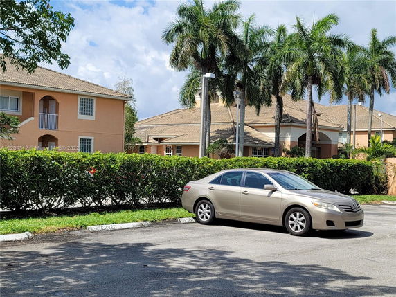 Outdoor parking area with a car parked in front of residential buildings and palm trees.