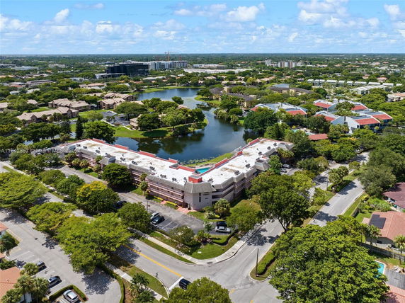 Aerial view of a residential area with a large building near a lake, surrounded by greenery and roads.