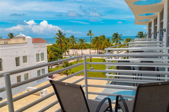 View from a balcony overlooking the ocean with palm trees and a sandy beach.