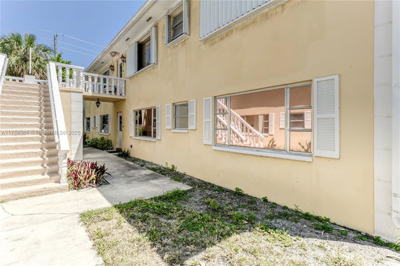 Side view of a yellow two-story house with stairs and shuttered windows