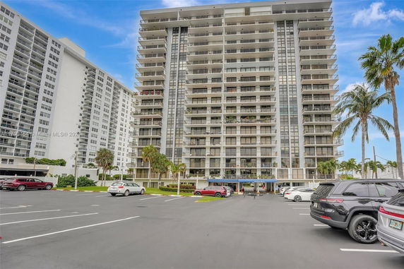 Front view of a high-rise apartment building with balconies and a parking area.