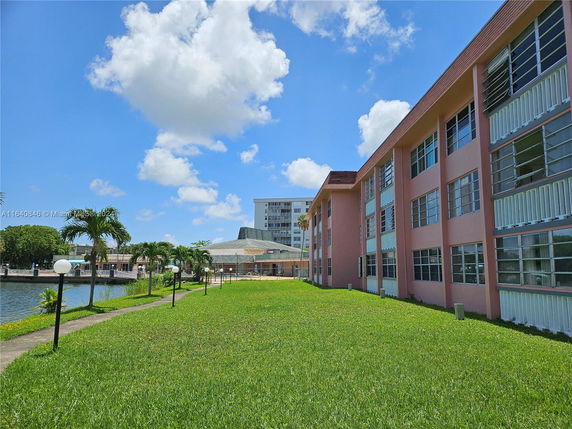 View of a building and green lawn area adjacent to a water body under a blue sky.