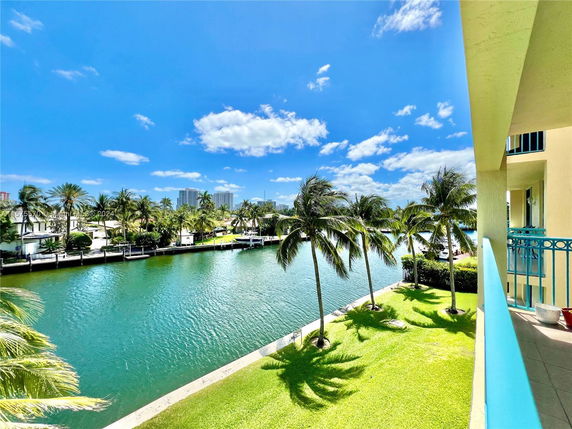 Wide angle view from a balcony overlooking a canal and palm trees with distant buildings.