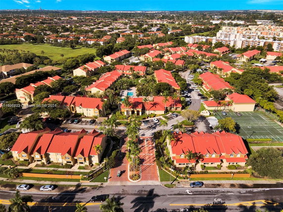 Aerial view of a residential area with multiple buildings featuring red roofs surrounded by greenery and roads.