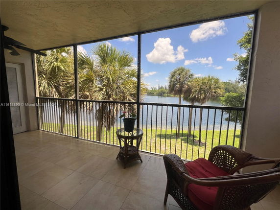 Balcony with wicker chairs overlooking a lake and palm trees.