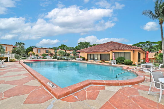 Outdoor swimming pool surrounded by a patio with chairs and umbrellas.
