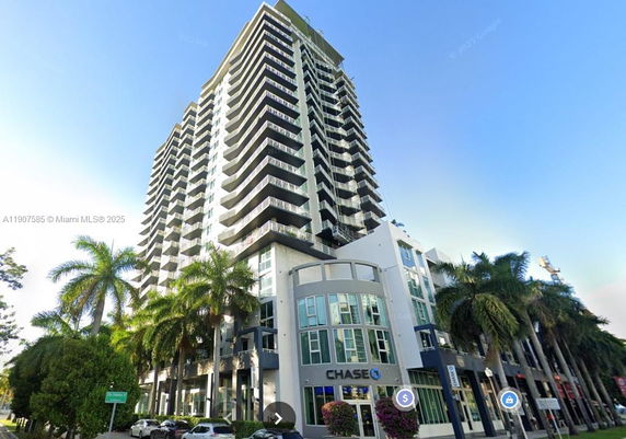 Front view of a tall multi-story building with balconies and ground-level commercial space.