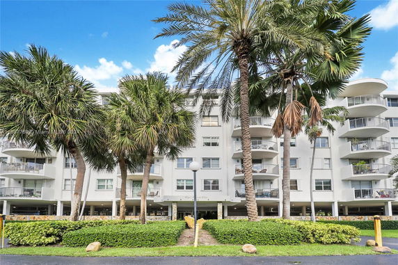 Front view of a multi-story building with balconies and surrounding palm trees.
