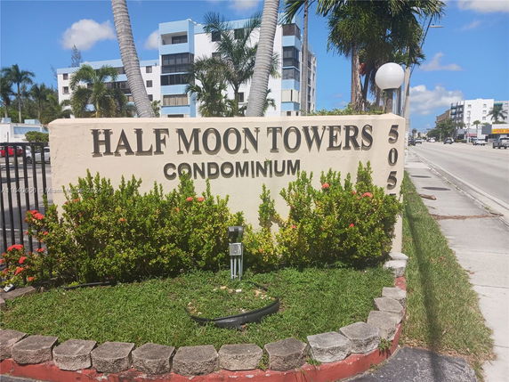 Sign for Half Moon Towers Condominium with building in background.