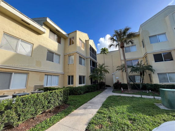 Front view of a multi-story building with external walkways and palm trees.