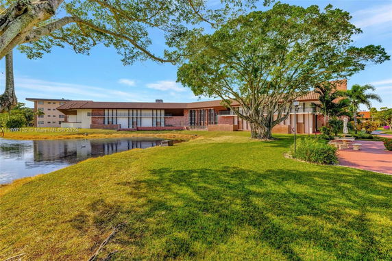 Front view of a two-story house with a large tree and a pond in the foreground.
