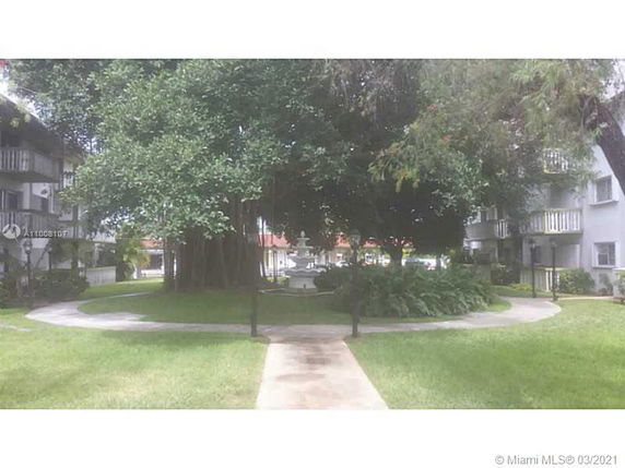 Outdoor area with a walking path, large trees, and surrounding buildings.