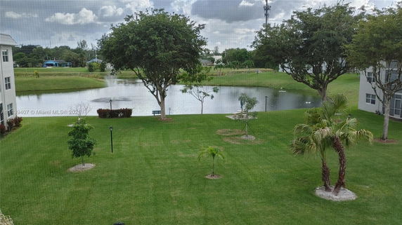 View of a grassy lawn with trees and a pond in the background surrounded by buildings.
